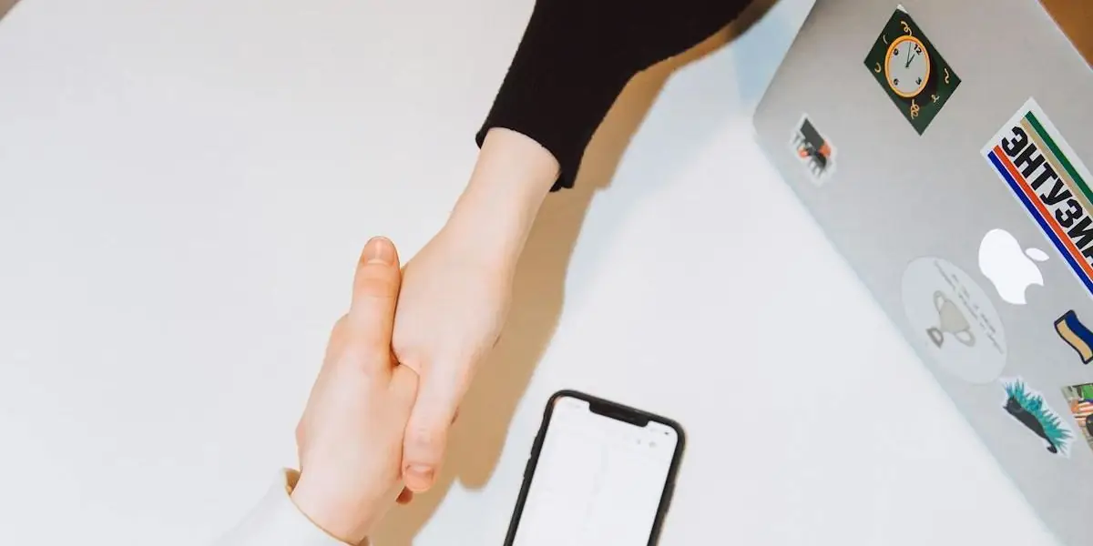 Zwei Hände schütteln sich über einem Schreibtisch mit Smartphone und Notizen