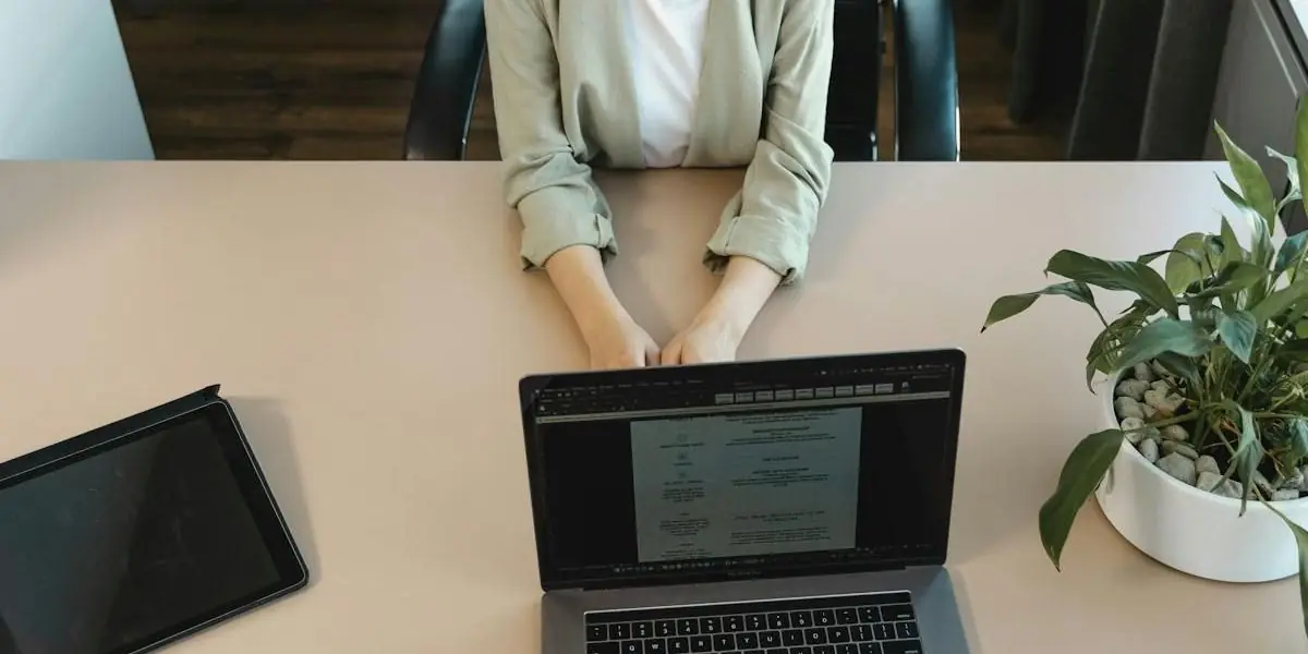Eine Bewerberin sitzt an einem Schreibtisch mit Laptop und Unterlagen gegenüber einer Gesprächsperson